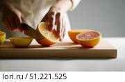 Chef skillfully slicing fresh oranges and grapefruits on a wooden cutting board, preparing vibrant ingredients for a colorful and nutritious dish bursting with flavor. Стоковое AI-изображение, AI-художник Юрий Поздников / Фотобанк Лори