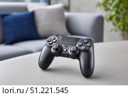 Modern black wireless gamepad resting on a table in a cozy living room, inviting gamers for exciting play sessions and providing a perfect blend of comfort and technology. Стоковое AI-изображение, AI-художник Юрий Поздников / Фотобанк Лори