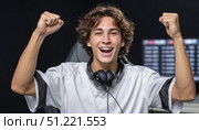 Triumphant male gamer wearing wireless headphones, celebrating competitive win with raised fists, expressing jubilant energy from successful esports tournament performance. Стоковое AI-изображение, AI-художник Юрий Поздников / Фотобанк Лори