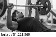 Muscular male weightlifter pressing heavy barbell during strength workout, displaying powerful chest muscles in contemporary fitness center. Стоковое AI-изображение, AI-художник Юрий Поздников / Фотобанк Лори