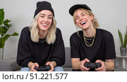 Female gamers sitting side by side on couch, playing video games and sharing joyful laughter during competitive gaming session. Стоковое AI-изображение, AI-художник Юрий Поздников / Фотобанк Лори