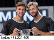 Male athletes beaming with pride, clutching silver trophy, celebrating triumphant win after competitive event, embodying athletic success and mutual accomplishment. Стоковое AI-изображение, AI-художник Юрий Поздников / Фотобанк Лори