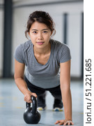 Determined young asian woman performing push ups with one hand resting on a kettlebell, exemplifying strength and dedication in a dynamic gym environment. Стоковое AI-изображение, AI-художник Юрий Поздников / Фотобанк Лори
