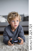 Boy lying on plush carpet, gripping wireless controller, playing videogame with intense blue eyed focus in sunlit living room. Стоковое AI-изображение, AI-художник Юрий Поздников / Фотобанк Лори