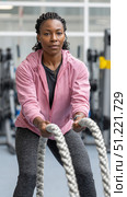 Determined sportswoman performing intense battle ropes exercise, showing strength and dedication during cross training workout at modern gym. Стоковое AI-изображение, AI-художник Юрий Поздников / Фотобанк Лори