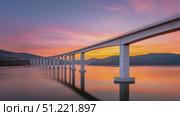 Concrete bridge crossing calm water, mirroring sunset hues with golden light washing over peaceful riverscape under soft pastel sky gradients. Стоковое AI-видео, аниматор Юрий Поздников / Фотобанк Лори
