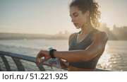 Urban fitness athlete tracking running performance, standing near ocean at sunset, holding water bottle, wearing wireless earphones during evening training session. Стоковое AI-видео, аниматор Юрий Поздников / Фотобанк Лори