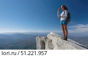 Female hiker standing on mountain peak, gesturing while absorbing expansive panoramic landscape with rolling hills, valleys stretching beneath luminous blue sky and distant horizon. Стоковое AI-видео, аниматор Юрий Поздников / Фотобанк Лори