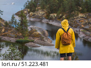 Tourism. Hiking. Ladoga skerries on Lake Ladoga. A tourist man in a yellow raincoat with a backpack on the rocky islands looks into the distance. Republic of Karelia, Russia. Стоковое фото, фотограф Photojuli / Фотобанк Лори