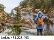 Tourism. Hiking. Ladoga skerries on Lake Ladoga. A female tourist in a raincoat with a backpack on the rocky islands looks into the distance. Republic of Karelia, Russia. Стоковое фото, фотограф Photojuli / Фотобанк Лори