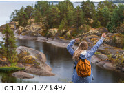 Tourism. Hiking. Ladoga skerries on Lake Ladoga. A female tourist in a raincoat with a backpack on the rocky islands looks into the distance. Republic of Karelia, Russia. Стоковое фото, фотограф Photojuli / Фотобанк Лори