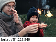 Children celebrating with colorful sparklers while dressed in warm clothing attire. Kids siblings enjoy the winter holidays outdoors. Festive evening. Christmas. New Year. Family Milestone Celebration. Стоковое фото, фотограф Марина Демидюк / Фотобанк Лори