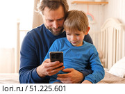 Father and son little boy laughing and using phone. They watching funny videos together, playing games on smartphone. Concept technology, smart phone addicted. Fun weekend activity. Modern fatherhood. Стоковое фото, фотограф Марина Демидюк / Фотобанк Лори