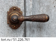 Antique Door Knob. Ornate wooden door with intricate carving metal handle. Faded gray wood. Elaborately fancy cabinet. Old furniture. Traditional architecture design. Decorative wrought iron metalwork. Стоковое AI-изображение, AI-художник Марина Демидюк / Фотобанк Лори