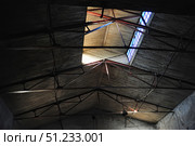 An old roof of an industrial building with wooden paneling and metal beams. Light penetrates through rectangular windows at the top of the roof, creating a contrast between the dark areas of the room and the illuminated details. The surface of the boards shows signs of time - darkening, roughness and traces of moisture. The metal structures, crossing each other, form a geometric pattern, giving the frame an industrial aesthetic. The atmosphere of the frame is reminiscent of abandoned workshops or warehouses, preserving the historical character of the space. Стоковое фото, фотограф Анна Кривицкая / Фотобанк Лори