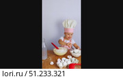 A little girl in a chef's hat and apron pours flour from a bowl into a dough with a spoon. On the table are a whisk, eggs, flour. Стоковое видео, видеограф Anna Scherbina / Фотобанк Лори