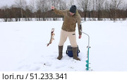 Fisherman pulls pike fish out of hole in ice during winter fishing on lake, next to him are spiral ice auger and fishing box. Стоковое видео, видеограф Владимир Григорьев / Фотобанк Лори