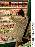 Person Browsing Through a Refrigerator Display Filled with Various Packaged Foods and Beverages in a Grocery Store Aisle. Стоковое фото, фотограф Владимир Федоров / Фотобанк Лори
