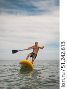 Energetic male on yellow paddle board tries to stay balanced while surfing waves. His joyful expression and intense movement capture freedom and humor of outdoor water sport. Стоковая иллюстрация, иллюстратор Енваев Андрей / Фотобанк Лори