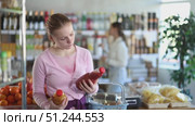 Young woman chooses freshly squeezed tomato and peach juice in glass bottles in a supermarket against the backdrop of buyers. Стоковое видео, видеограф Яков Филимонов / Фотобанк Лори