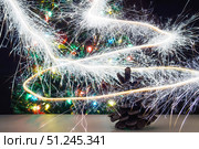 Fir cone with sparkler freezelight around on background christmas tree with garland lights. Selective focus. Стоковое фото, фотограф Зарифа Арсланова / Фотобанк Лори