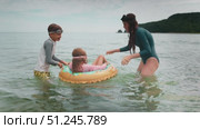 Childs enjoy time in shallow sea water, playing with float ring. Scene captures bonding family, joy and outdoor fun. Happy family moment during summer vacation, filled with laughter and love. Стоковое видео, видеограф Енваев Андрей / Фотобанк Лори