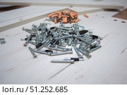 Furniture fasteners are poured out in a pile on furniture parts. Стоковое фото, фотограф Екатерина Кузнецова / Фотобанк Лори