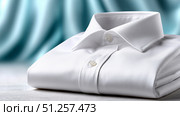 Perfectly folded white shirt on a wooden surface with a blurred background. Стоковое AI-изображение, AI-художник Katsiaryna Repich / Фотобанк Лори