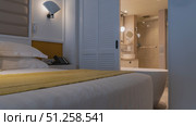 The bed is covered with white sheets, a yellow bedspread. Pillows at the headboard. The wall sconce is lit. The bathroom behind the open louvered partition. Bathtub, shower stall, mirror, washbasin. Стоковое фото, фотограф Вера Ивановна Кубарева / Фотобанк Лори