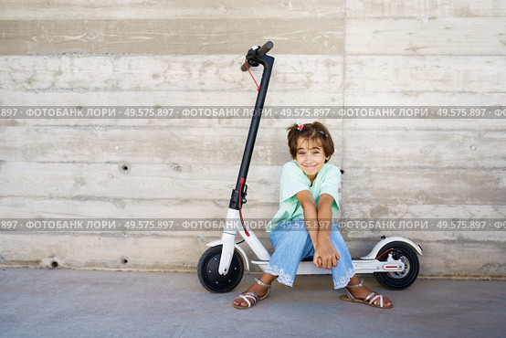 9-year-old girl sitting on an electric scooter in the street. Little girl sitting on an electric scooter in the street. Стоковое фото, агентство Ingram Publishing / Фотобанк Лори