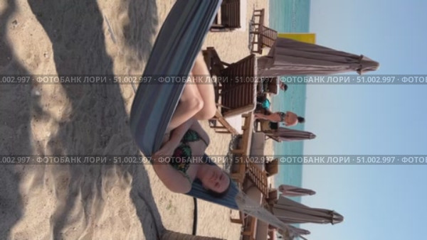A 50-year-old woman on the beach in Doha is riding a hammock. Стоковое видео, видеограф IRYNA ZAKHARANKA / Фотобанк Лори