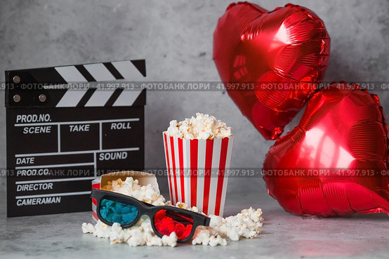 A banner for the film industry. A romantic movie date. A movie camera, 3D glasses, popcorn and foil balloons in the shape of hearts on a concrete gray background. The film will premiere on Valentine's Day. (2024 год). Стоковое фото, фотограф Photojuli / Фотобанк Лори