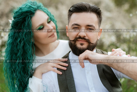a bearded groom plays a stringed instrument and a girl with green hair sits in a spring meadow. Стоковое фото, агентство Ingram Publishing / Фотобанк Лори