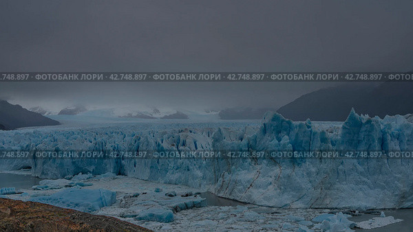 A beautiful blue glacier stretches to the horizon between the mountains. A mass of ice with cracks, crevices, and sharp peaks. Thawed ice floes float off a glacial lake. Cloudy. Fog. Perito moreno. Стоковое фото, фотограф Вера Ивановна Кубарева / Фотобанк Лори