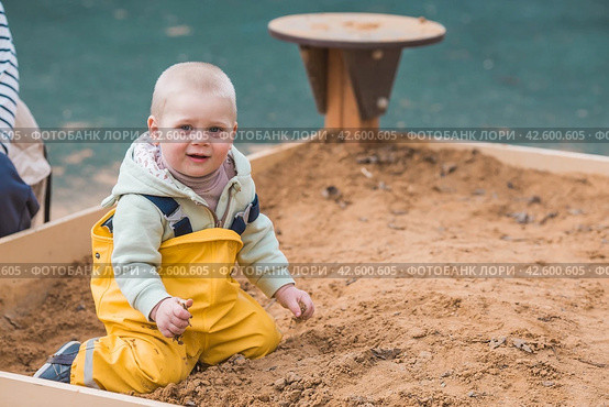 A beautiful, cheerful little boy of two years old walks on the playground in the spring. A child is playing with a shovel in the sandbox. The concept of parenthood, happy childhood and family. Стоковое фото, фотограф Photojuli / Фотобанк Лори