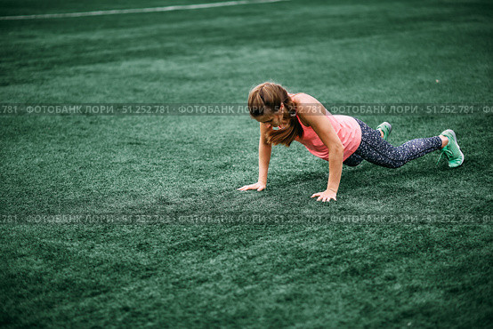 A beautiful muscular girl in leggings and a vest makes a burpee at the stadium. Cross fit, fitness, healthy lifestyle. Стоковое фото, фотограф Арзюков Вадим Николаевич / Фотобанк Лори