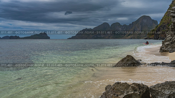 A beautiful secluded beach on a tropical island. Picturesque boulders by the water. Foam of waves on the sand. Tourist canoe in the turquoise ocean. Mountains on the horizon. Clouds in the sky. Стоковое фото, фотограф Вера Ивановна Кубарева / Фотобанк Лори