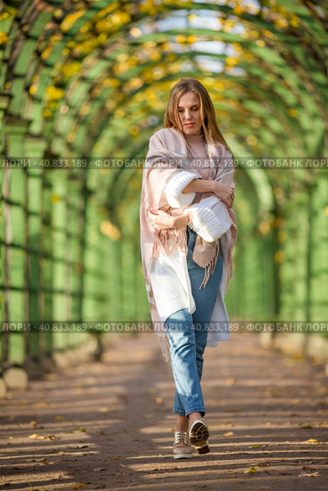 A beautiful young woman with light brown hair walks along a picturesque alley in an autumn park. An attractive woman wrapped herself in a plaid. Fall season. Thoughtful and melancholic autumn mood. Стоковое фото, фотограф Андрей Степанов / Фотобанк Лори