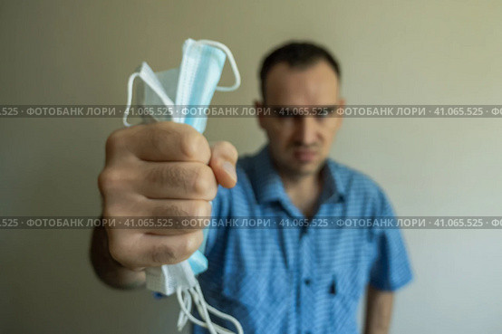 A blurry photo of a Caucasian man clutching medical masks in his hand. Gray background. Opposition to the mask regime and vaccination. Protest against wearing a mask. Стоковое фото, фотограф Воловодов Владимир / Фотобанк Лори