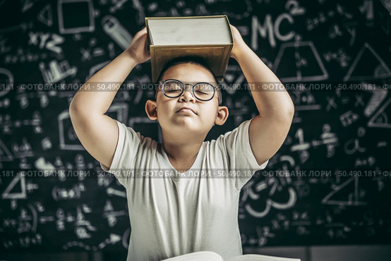 A boy with glasses studied and put a book on his head in the classroom. Стоковое фото, агентство Ingram Publishing / Фотобанк Лори