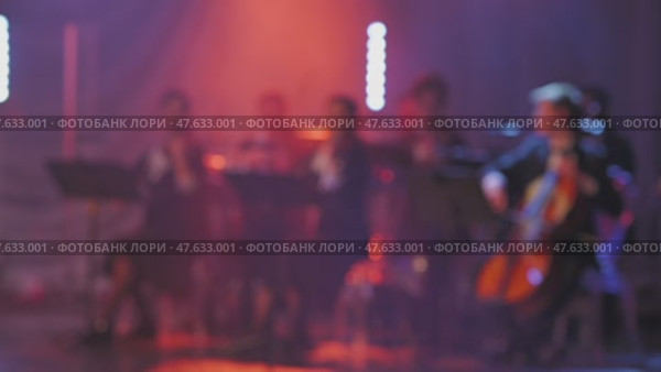 A breathtaking scene of musicians performing with violins and cello under bright, colorful lighting. The blurred view enhances the focused energy of the music being performed. Стоковое видео, видеограф Воловодов Владимир / Фотобанк Лори