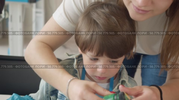 A caring young art teacher assists a boy in creating drawings on clothing during a master class. Стоковое видео, видеограф Strunov David / Фотобанк Лори