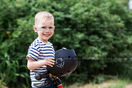 A cheerful little boy rides a running bike in a helmet outdoors. A happy child is engaged in an active sport. Protection. Life insurance and child safety. Стоковое фото, фотограф Photojuli / Фотобанк Лори