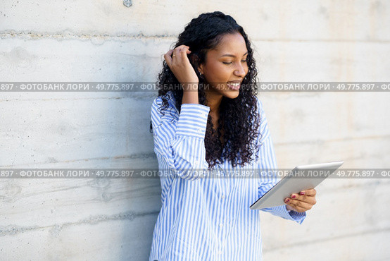 A cheerful young woman in a colorful striped shirt is engaged with her tablet, showcasing her enthusiasm for modern technology and the resources it provides for her daily activities. A Happy Young Woman Engaged with Her Tablet in a Stylish and Modern Indoor Setting. Стоковое фото, агентство Ingram Publishing / Фотобанк Лори