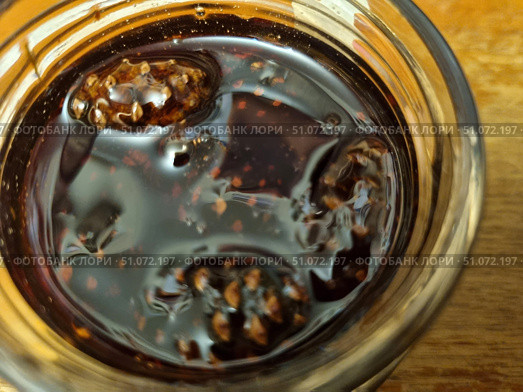 A close-up of a jar of pine cone jam, clearly showing the small young pine cones submerged in a thick, dark amber syrup. The shiny surface of the syrup reflects the light, creating a delicious and inviting appearance. You can see how the seeds and texture of the pine cones contrast with the smooth consistency of the sweet liquid. Pine cone jam is known for its rich, pine-like aroma and health benefits - it is often used as a treat and as a natural remedy for supporting the immune system. The image is perfect for illustrations of recipes, publications on canning, cooking, traditional medicine and natural products. Стоковое фото, фотограф Анна Кривицкая / Фотобанк Лори