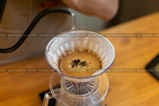 A close-up of coffee brewing in a pour-over dripper. The coffee grounds are dark and wet, with a rich brown liquid dripping into a clear carafe below. Стоковое фото, фотограф PAv / Фотобанк Лори