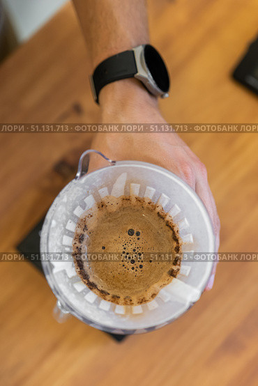 A close-up view of a hand pouring coffee through a filter into a brewing device. The scene features a wooden table and a modern coffee setup. Стоковое фото, фотограф PAv / Фотобанк Лори