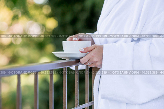 A cup of hot tea in the hands of a girl in a white coat. Morning of the bride. The concept of staying at the hotel and starting the wedding day. Стоковое фото, фотограф Photojuli / Фотобанк Лори