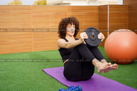 A dedicated woman performs an intense core workout on an outdoor yoga mat with a weight plate, emphasizing the importance of fitness and a healthy lifestyle for overall wellbeing. A dedicated fitness enthusiast is performing an intense core workout utilizing a weight plate. Стоковое фото, агентство Ingram Publishing / Фотобанк Лори