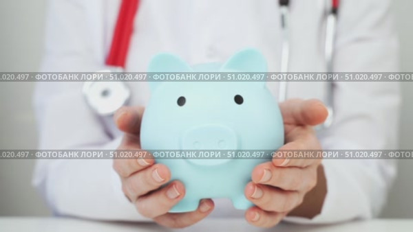 A Doctor Woman Holding a Piggy Bank in Her Hands. Concept of additional medical insurance. Lca. Стоковое видео, видеограф Igor Skripachev / Фотобанк Лори
